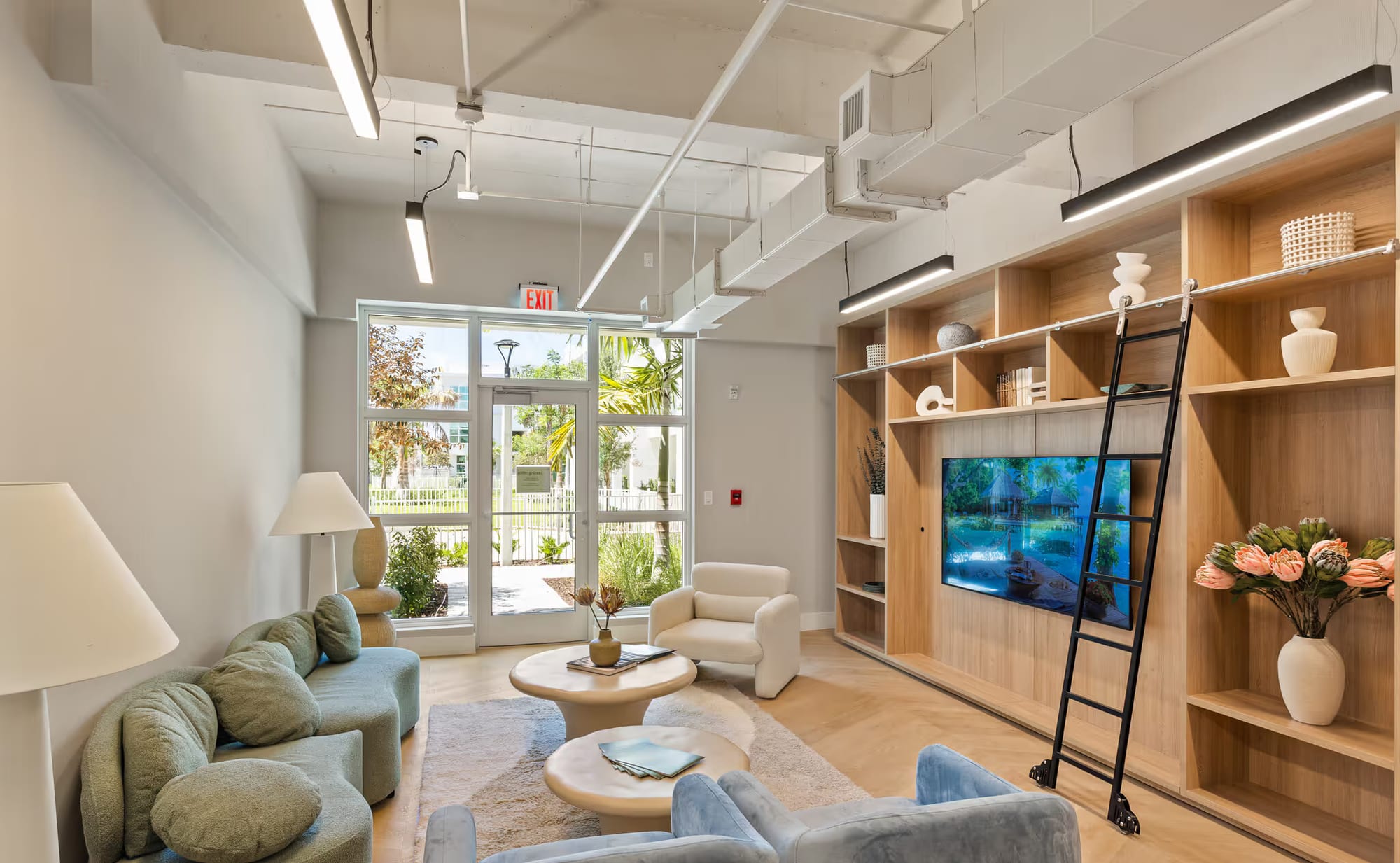The residents’ lounge — sage bouclé seating, a wood library wall, glass doors to the garden